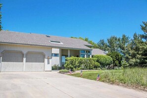 A single-story building with a garage, a small porch, and a well-maintained lawn with American flags. - Dog-friendly house with private heated outdoor pool, hot tub & Ping-Pong (Grand Beach)