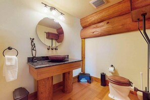 Une salle de bain avec un meuble-lavabo en bois, un miroir rond, un lavabo sur colonne, des toilettes et un porte-serviettes.