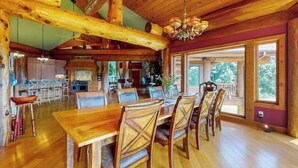 Een ruime eethoek met een houten tafel en stoelen, een kroonluchter en grote ramen.