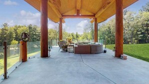 Een terras buiten met een houten pergola, een zithoek en uitzicht op een bebost landschap.