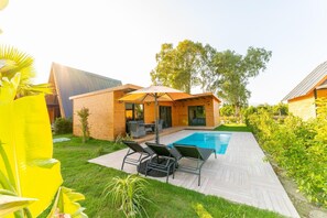 Une maison moderne dotĂ©e dâune piscine, de mobilier de jardin et dâun espace extĂ©rieur amĂ©nagĂ© et abritĂ©.
