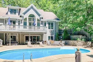 Ein zweistöckiges Haus mit Swimmingpool, einer überdachten Terrasse und einem Balkon.