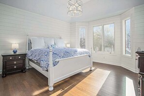Une chambre à coucher avec un lit, des tables de chevet, une lampe et de grandes fenêtres.