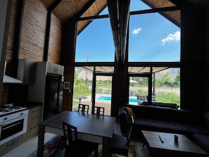 A modern kitchen with a dining area, large windows, and a view of a pool and mountains.