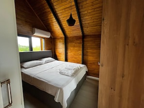 A bedroom with a wooden ceiling, a bed with white linens, a window, and an air conditioning unit.