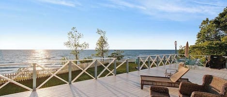 A wooden deck with outdoor furniture, a railing, and a view of the sea.
