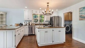 A spacious kitchen with white cabinetry, a central island, stainless steel appliances, and a chandelier.