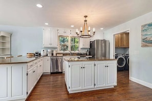 A spacious kitchen with white cabinetry, a central island, stainless steel appliances, and a chandelier.
