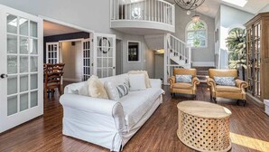 A spacious living area with a white sofa, two armchairs, a round wooden coffee table, and a balcony with a railing.