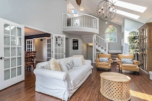 A spacious living area with a white sofa, two armchairs, a round wooden coffee table, and a balcony with a railing.