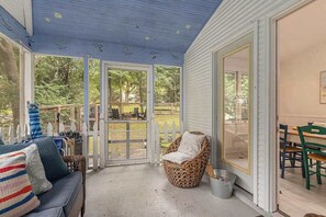 A covered porch with a sofa, wicker chair, and dining table. - Garden-style cottage with easy beach access, screened porch & small yard (Lakeside)