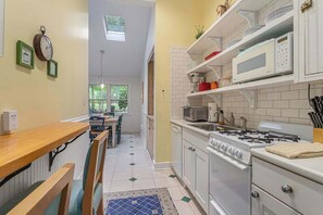 A compact kitchen with a dining area, a stove, microwave, and a window. - Garden-style cottage with easy beach access, screened porch & small yard (Lakeside)