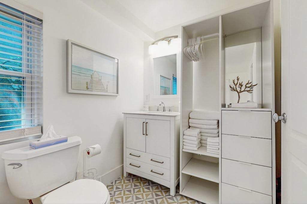Une salle de bain comprenant des toilettes, un lavabo, un meuble de rangement, un porte-serviettes et un tableau encadré au mur.