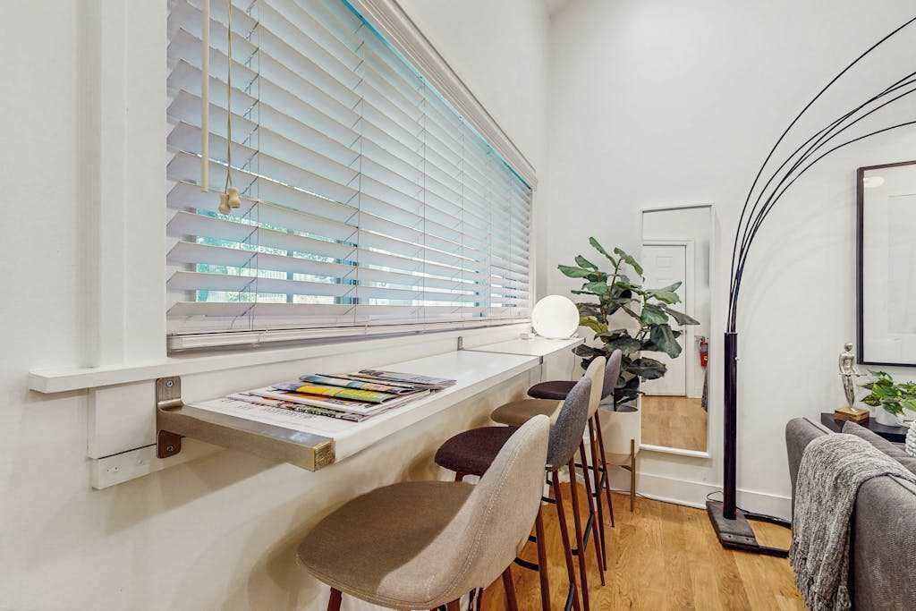 A modern interior with a bar area, seating, and a large window with blinds.