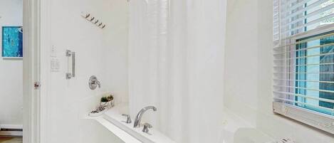 A modern bathroom with a bathtub, a shower curtain, a window with blinds, and a towel rack.