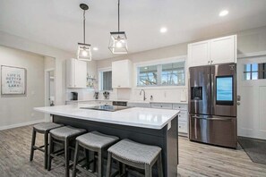 A modern kitchen with a large island, stainless steel appliances, and pendant lighting. - Modern home with large sun-room, firepit, grill, washer/dryer, & central AC (Sawyer)