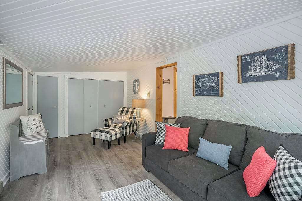 Un salón acogedor con un sofá gris, sillones a cuadros, una mesita y una ilustración de un barco colgado en la pared.