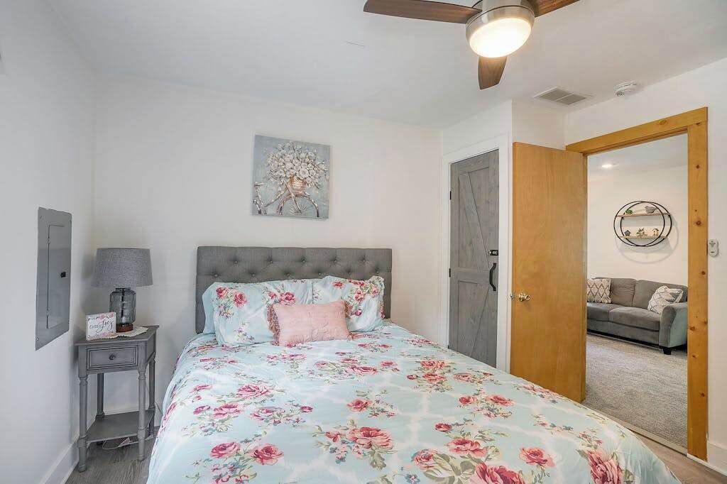 Une chambre à coucher comprenant un lit, une table de chevet, un ventilateur de plafond, une porte et un coin salon avec un canapé.