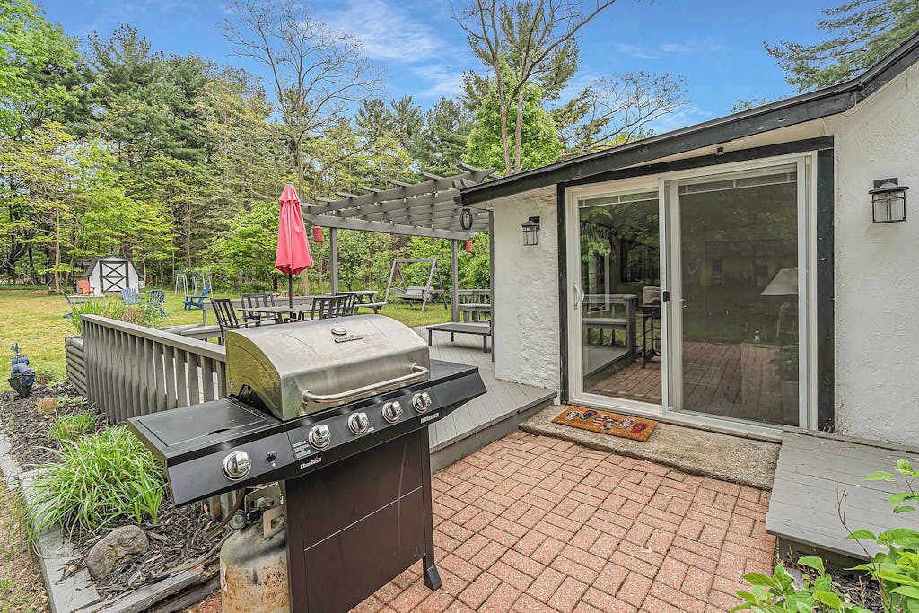 A backyard with a grill, patio furniture, and a covered seating area.