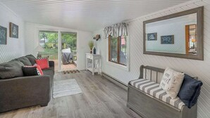 Een gezellige woonkamer met een bank, een lange zitbank en een kleine tafel. Er is een raam met gordijnen en een spiegel aan de muur.