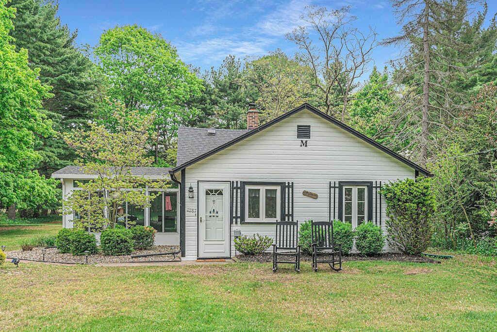 A single-story house with a white exterior, a chimney, and a front porch with two chairs.