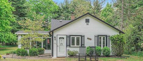 A single-story house with a white exterior, a chimney, and a front porch with two chairs.
