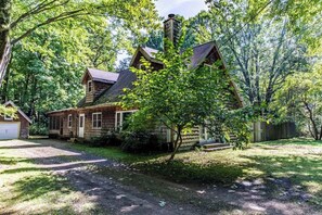 A wooden cabin with a chimney, surrounded by trees and a grassy yard. - Dog-friendly home w/private heated pool, free WiFi, gas grill, & washer/dryer (Three Oaks)