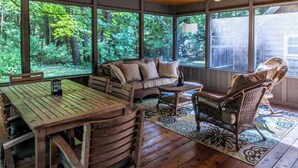 Un portico coperto con mobili in legno, ampie finestre e vista su una foresta.