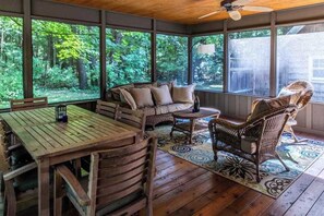 A covered porch with wooden furniture, large windows, and a view of a forest. - Dog-friendly home w/private heated pool, free WiFi, gas grill, & washer/dryer (Three Oaks)