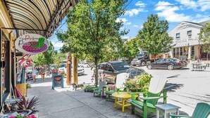 Vista de la calle con mesas al aire libre, un letrero que dice 'The Pink Patio' y un edificio con fachada blanca.