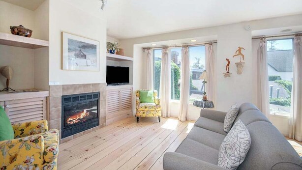 Una sala de estar con chimenea, un sofá, un televisor y un ventanal con cortinas.