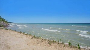 A beach with clear water, sandy shore, and sparse vegetation. - Gorgeous home w/ furnished patio, decks, & open living space - easy beach access (South Haven)