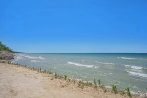 A beach with clear water, sandy shore, and sparse vegetation. - Gorgeous home w/ furnished patio, decks, & open living space - easy beach access (South Haven)
