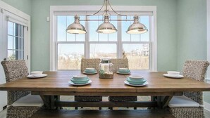 A dining area with a wooden table, wicker chairs, and a view through large windows. - Gorgeous home w/ furnished patio, decks, & open living space - easy beach access (South Haven)