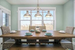 A dining area with a wooden table, wicker chairs, and a view through large windows. - Gorgeous home w/ furnished patio, decks, & open living space - easy beach access (South Haven)