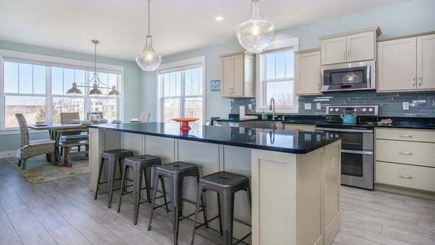 A kitchen with a large island, bar stools, a microwave, and a stove. - Gorgeous home w/ furnished patio, decks, & open living space - easy beach access (South Haven)