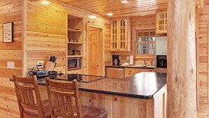 A wooden cabin interior with a kitchen area, wooden cabinets, a dining table with chairs, and a built-in microwave. - Cabin tucked in the trees with private hot tub & lake/pool access (Saugatuck)