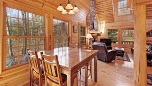 A wooden cabin interior with a dining table, chairs, a fireplace, and large windows. - Cabin tucked in the trees with private hot tub & lake/pool access (Saugatuck)