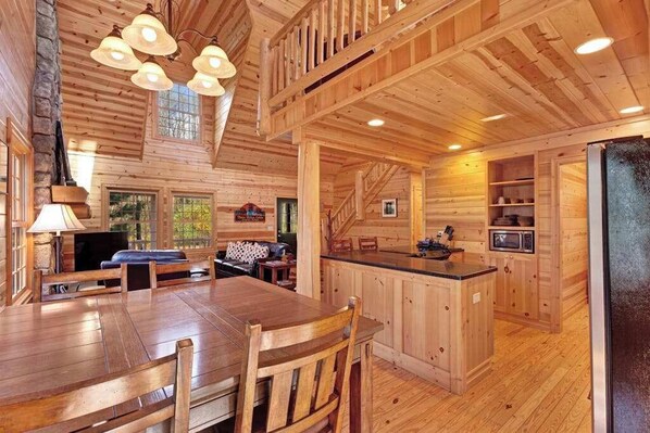 A wooden cabin interior with a dining area, kitchen, and a staircase.