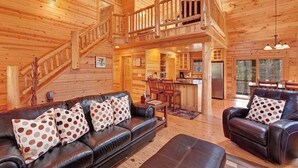 A spacious log cabin interior with a living room, dining area, kitchen, and a staircase leading to an upper level. - Cabin tucked in the trees with private hot tub & lake/pool access (Saugatuck)