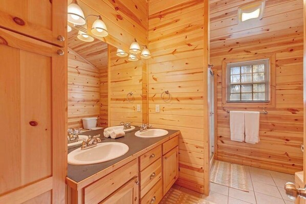 Ein Badezimmer in einer Holzhütte mit zwei Waschbecken, einem großen Spiegel und einem Fenster mit Jalousien.
