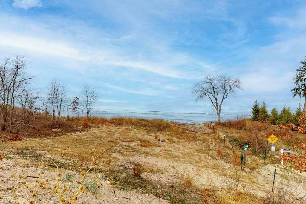 A coastal landscape with a dirt path, sparse vegetation, and a clear sky.