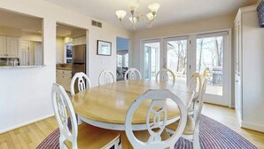 Comedor con mesa de madera y sillas blancas, un candelabro y vistas a través de amplios ventanales.