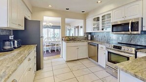 Una cocina moderna con gabinetes blancos, horno empotrado, microondas y una zona de comedor con mesa y sillas.