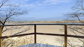 Una terraza de madera con vistas a una playa con dunas arenosas y un cielo despejado.