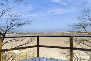 A wooden deck overlooking a beach with sandy dunes and a clear sky.