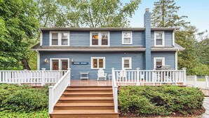 Uma casa de dois andares com varanda, grades brancas e uma placa que diz 'Beach House'.