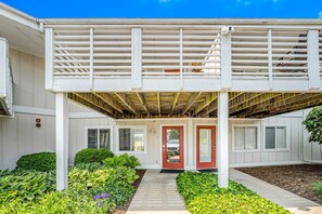 A covered porch with a red door, white railings, and a small garden area with various plants. - Updated condo with well-equipped kitchen, pool, firepits, grill, & gas fireplace (Douglas)