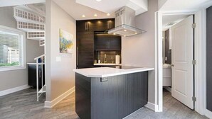 Een moderne keuken met een centraal eiland, geïntegreerde apparatuur en een trap.