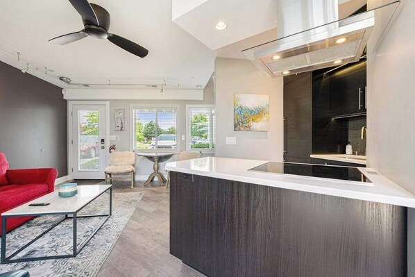 A modern kitchen with a central island, a ceiling fan, and a dining area with a red sofa and a coffee table. - Updated condo with well-equipped kitchen, pool, firepits, grill, & gas fireplace (Douglas)